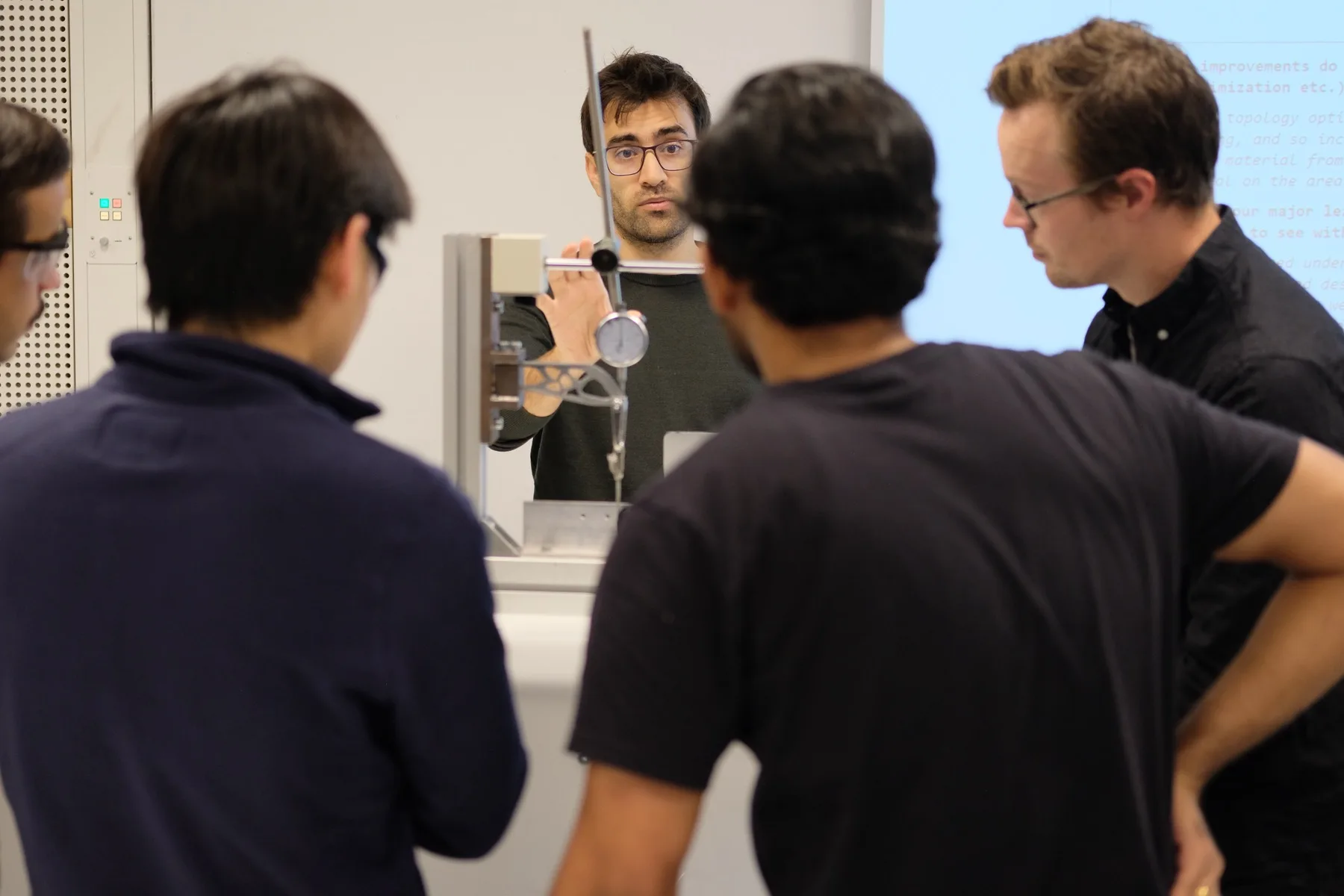 A student demonstrating a 3D-printed lattice bracket on a tensile testing rig to classmates during a lab session